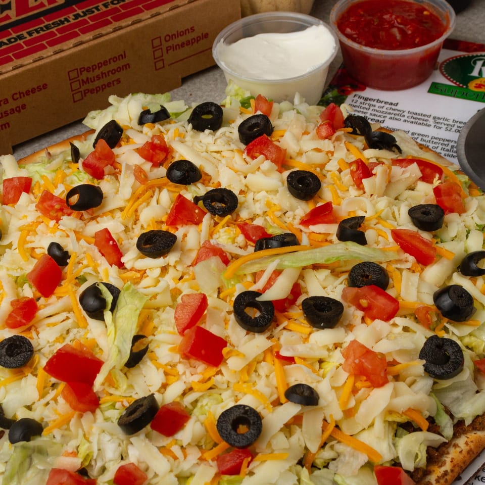 Rounders Pizza's taco pizza, topped with shredded lettuce, cheese, diced tomatoes, and black olives.