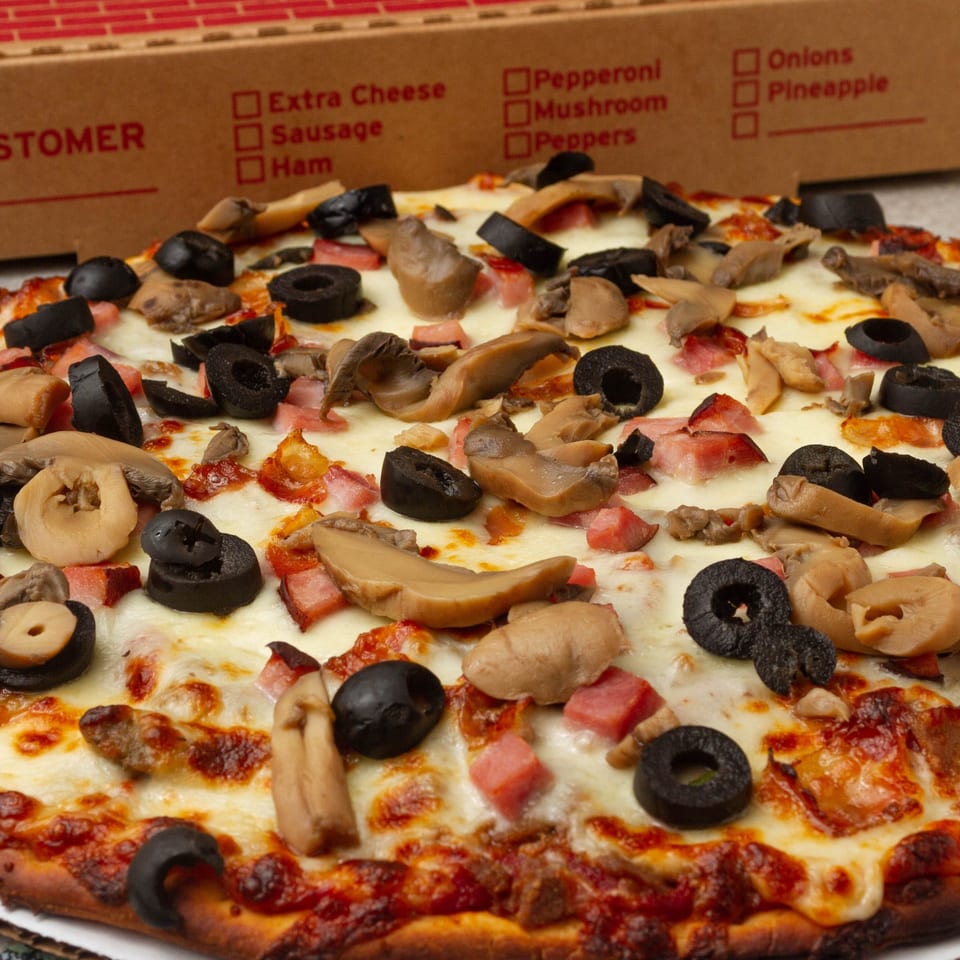 Rounders Pizza with mushrooms, black olives, and ham, with a pizza box in the background.