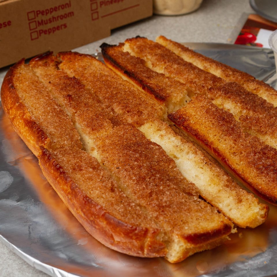 Rounders Pizza cinnamon breadsticks, golden brown and sugar-dusted, on aluminum foil.