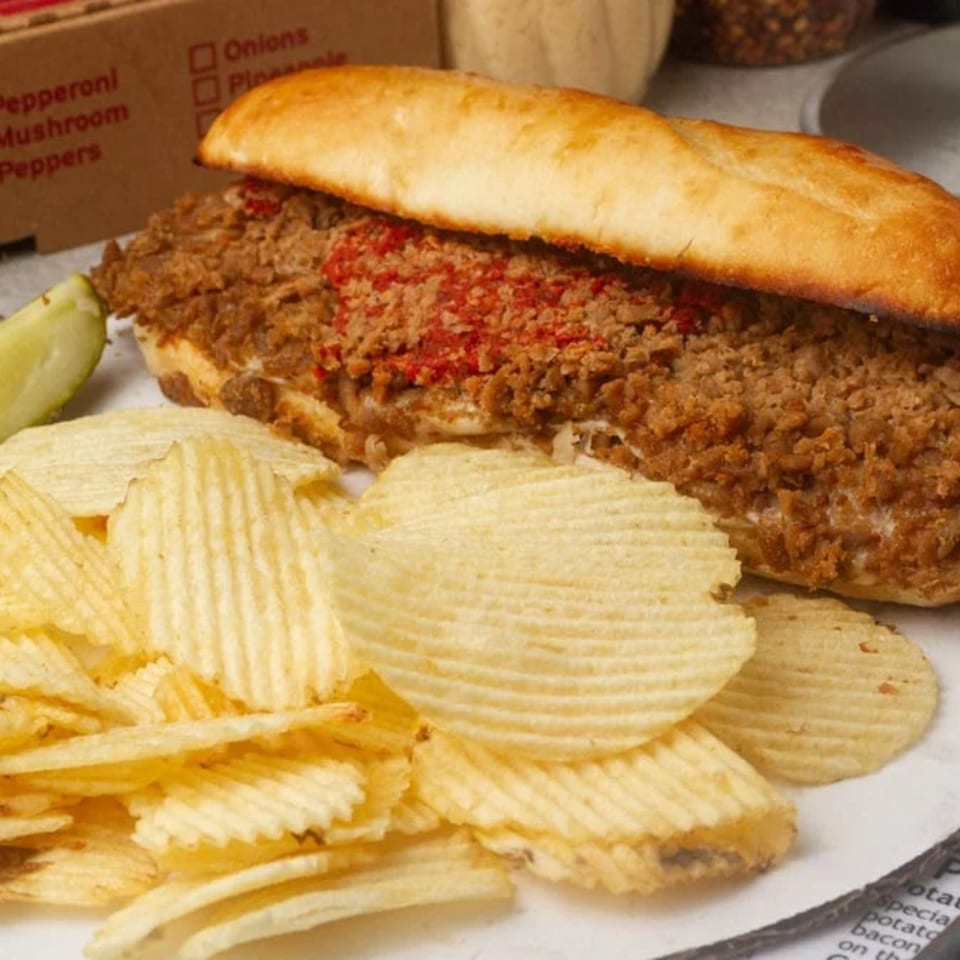 A Rounders Pizza sub sandwich with meat and red sauce, served with ridged potato chips.